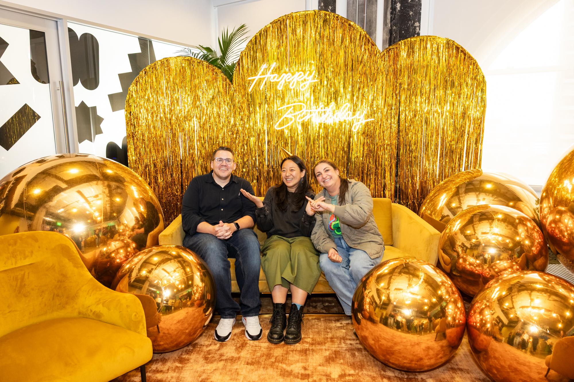 Mingjin on a yellow sofa with mentor and manager in front of a gold tinsel backdrop.
