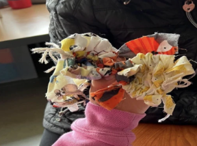 A student holding up her finished woven creation, used as a bowtie for her pet.